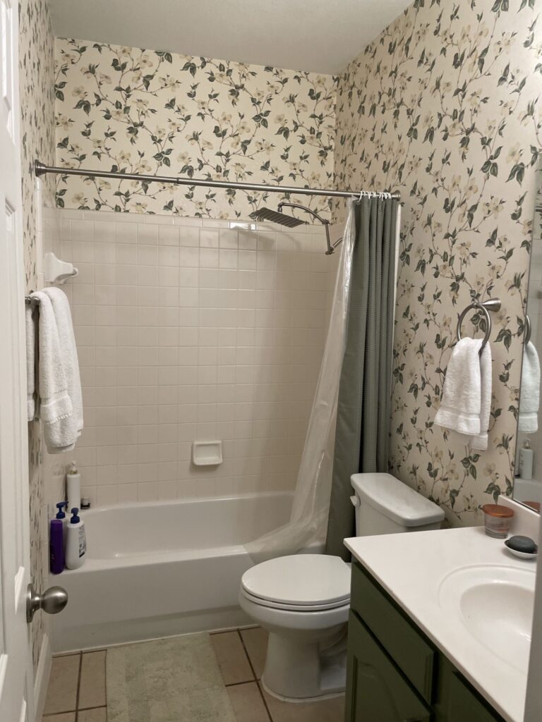 Before: dated bathroom with tub and shower combination and floral wallpaper, before a Heritage remodel