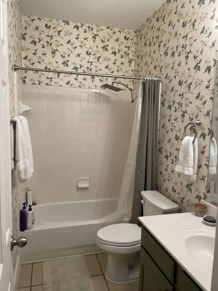 Before: dated bathroom with tub and shower combination and floral wallpaper, before a Heritage remodel