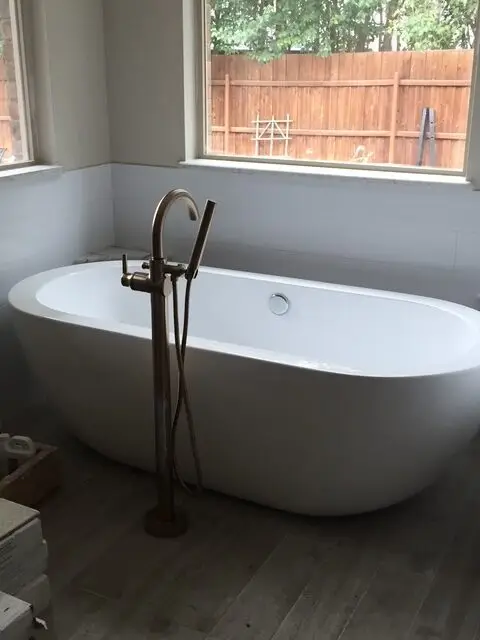 Freestanding oval tub beneath a window with bronze floor-mount filler