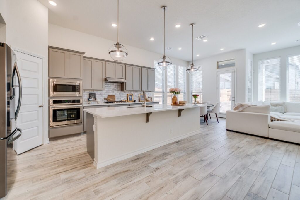 Light gray kitchen with long island, pendant lights and wood-look floors