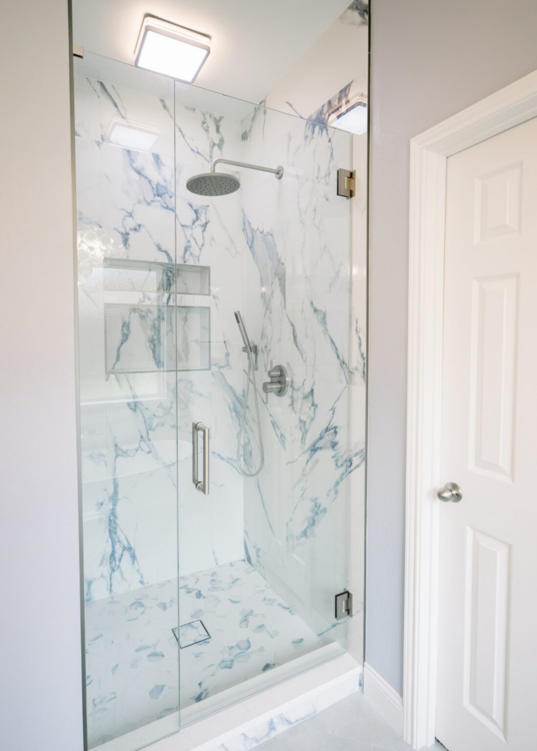 Walk-in shower with blue-veined marble-look tile, hexagon mosaic floor and frameless glass door, bathroom remodel in DFW