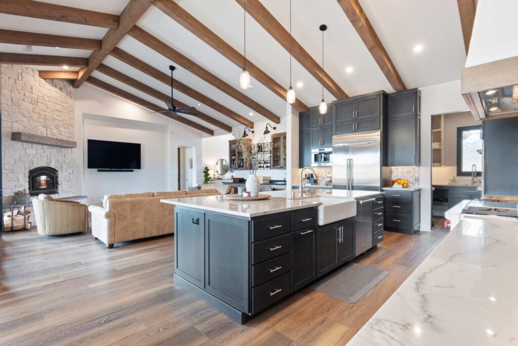 Open kitchen and living room with vaulted wood beams and dark cabinetry