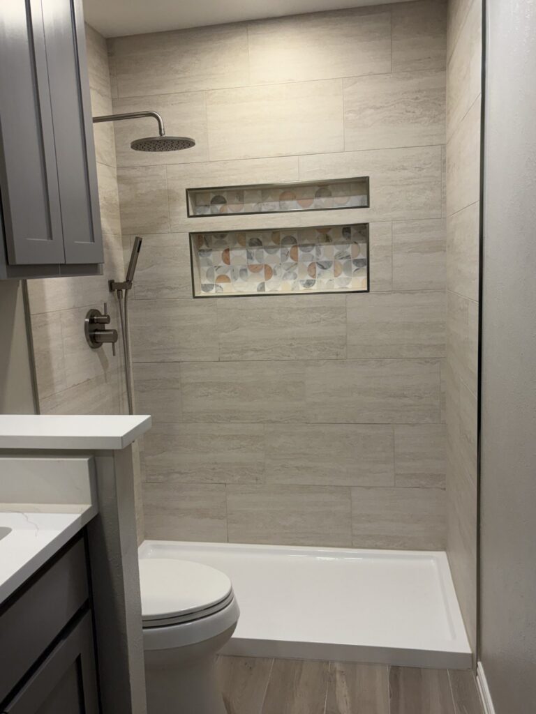 Tiled walk-in shower with mosaic niche beside a gray vanity, bathroom remodel in DFW