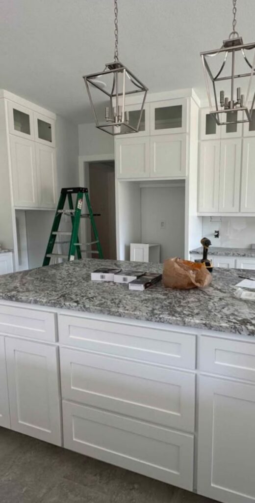 White kitchen cabinetry with lantern pendants and granite island during a kitchen remodel