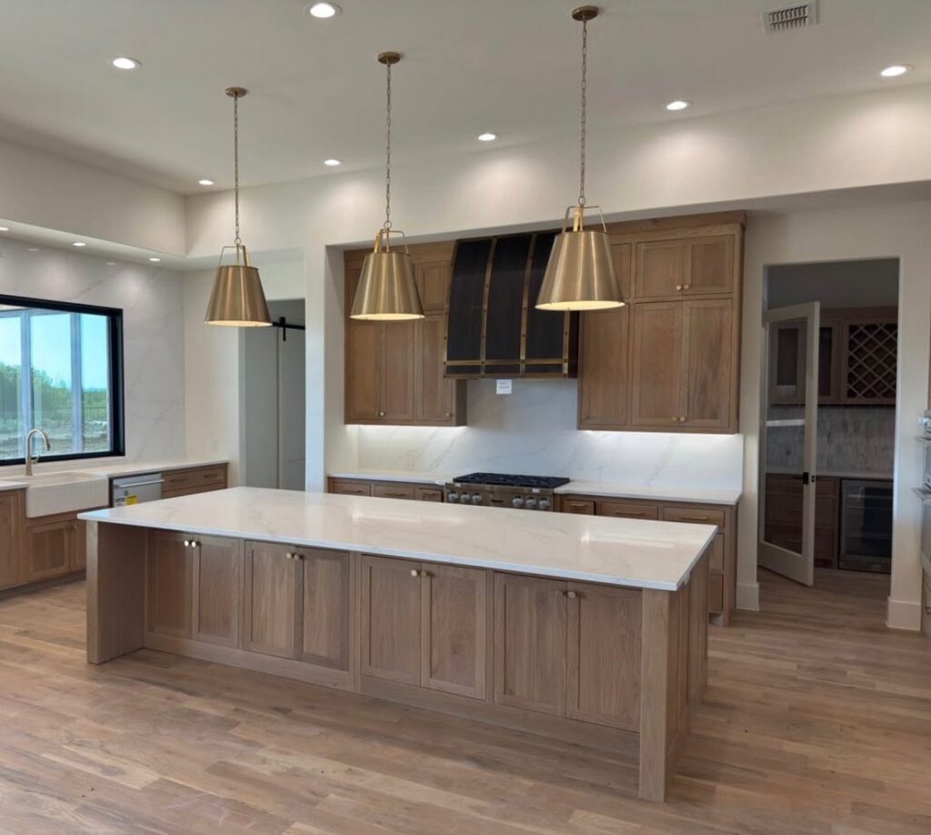 White oak kitchen with a large quartz island and brass pendant lights, kitchen remodeling by Heritage Remodelers & Builders in DFW